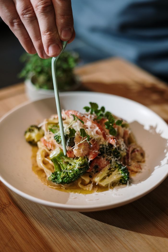 Delicious Italian pasta dish being garnished by hand, showcasing fresh ingredients.