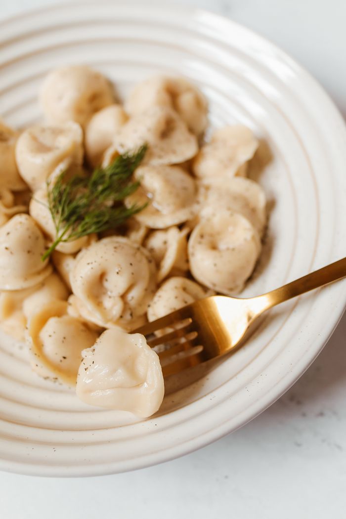 Close-up of traditional Russian pelmeni with dill, pepper, and a golden fork.